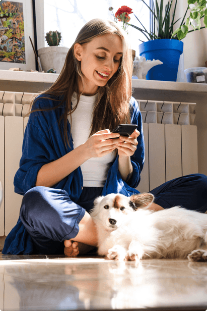 woman using cell phone while sitting on the floor with her dog