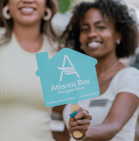 two women smiling with one woman holding an Atlantic Bay sign