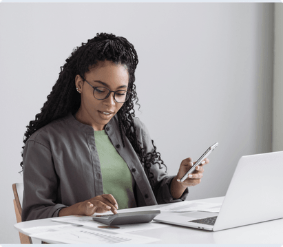 woman sitting at desk doing calculations using electronic devices
