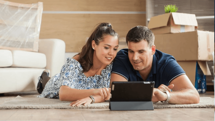 A couple lying down on a rug using a tablet