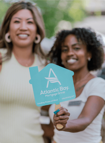 two women smiling with one woman holding an Atlantic Bay sign